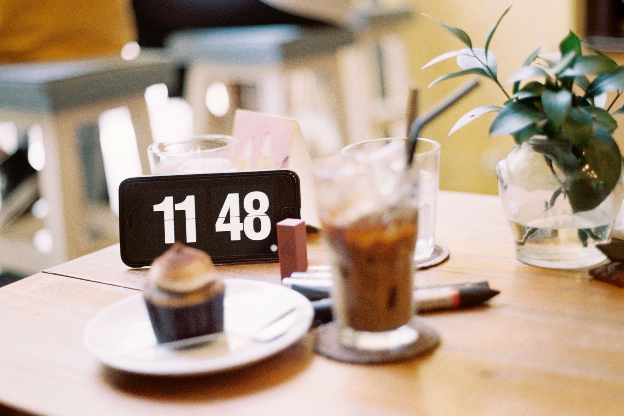 An image of a table with a cell phone, a plant, a cup, and a cupcake