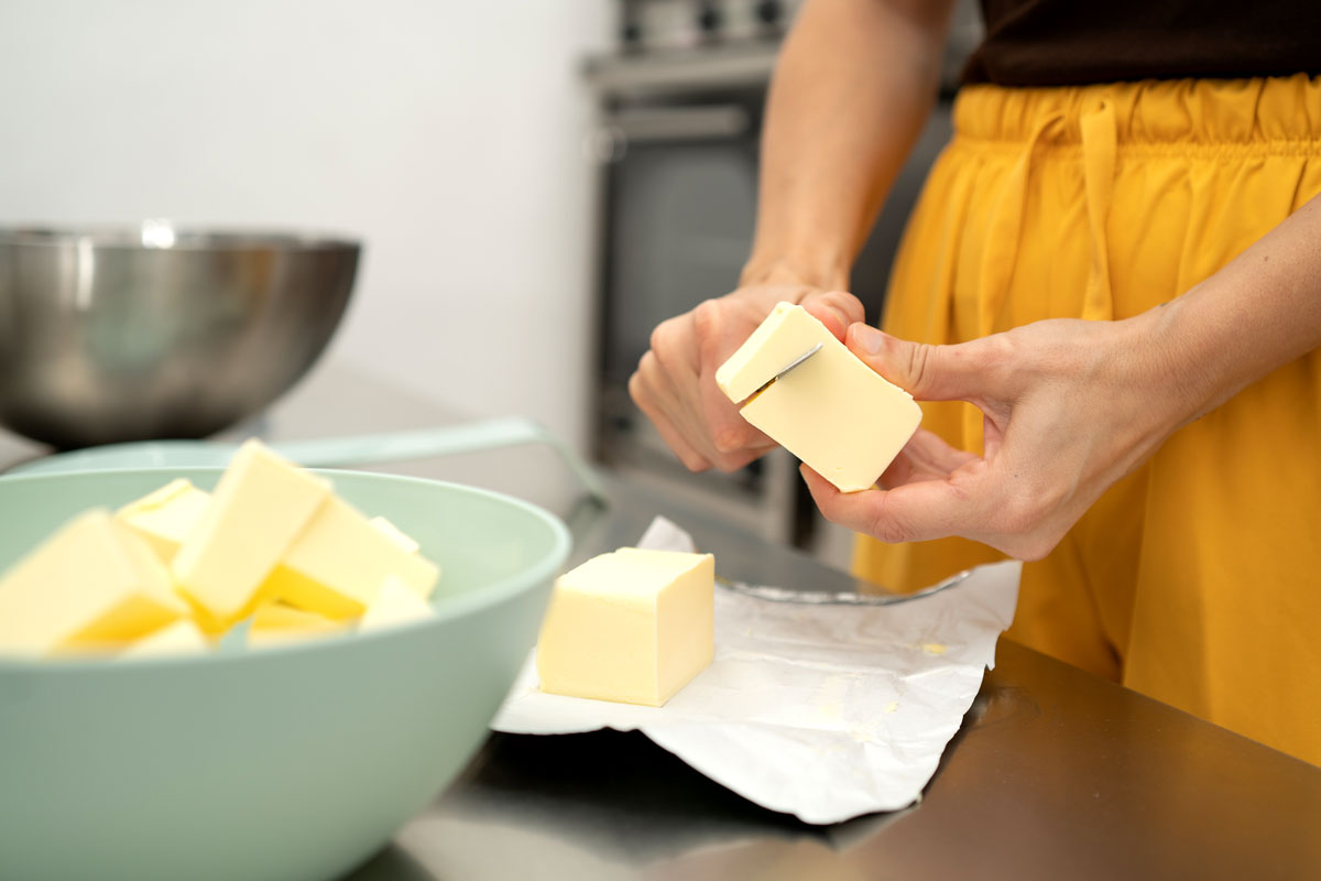 An image of hands cutting butter with a red knife in a kitchen