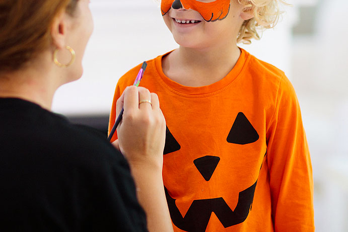 An image of a child getting their face painted by an adult