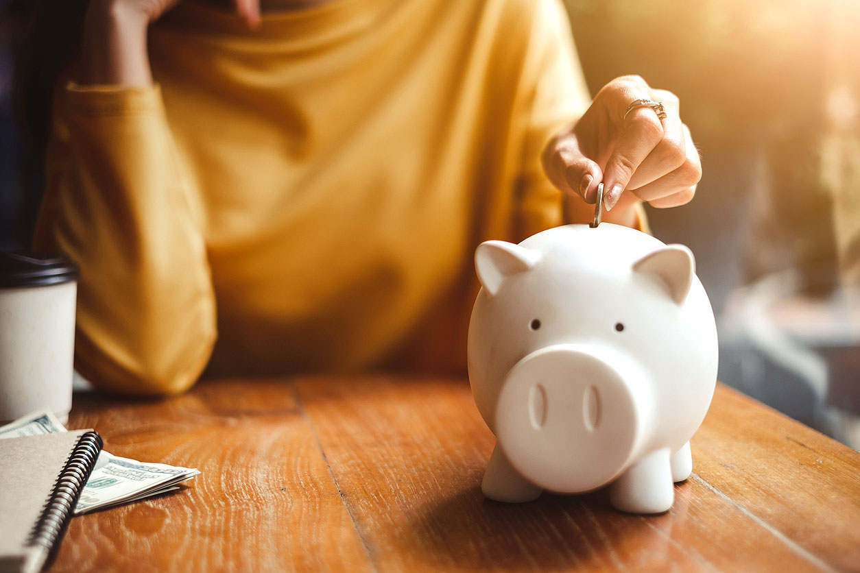 An image of a person putting a coin into a white piggy bank