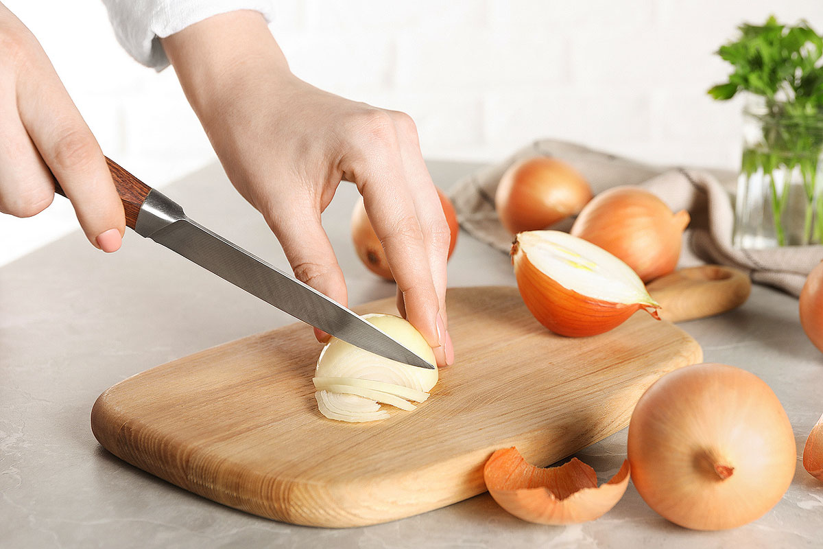 An image of a person slicing a white onion on a wood cutting board