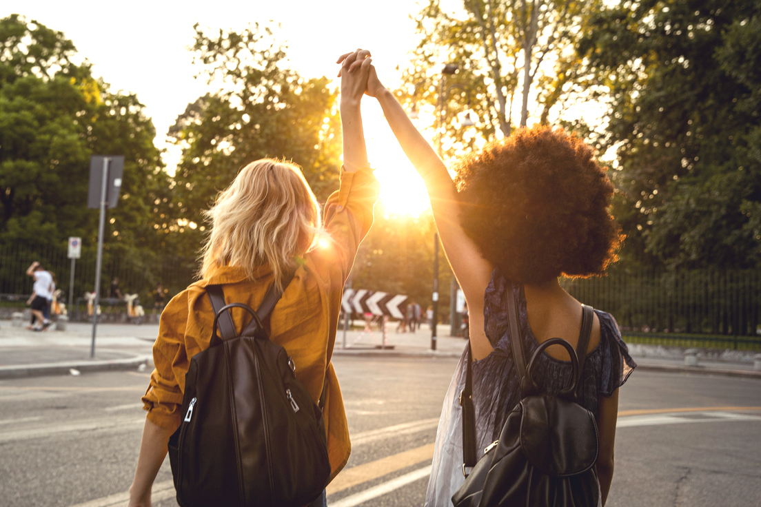 An image of two women holding hands in the air with the sun glaring between them