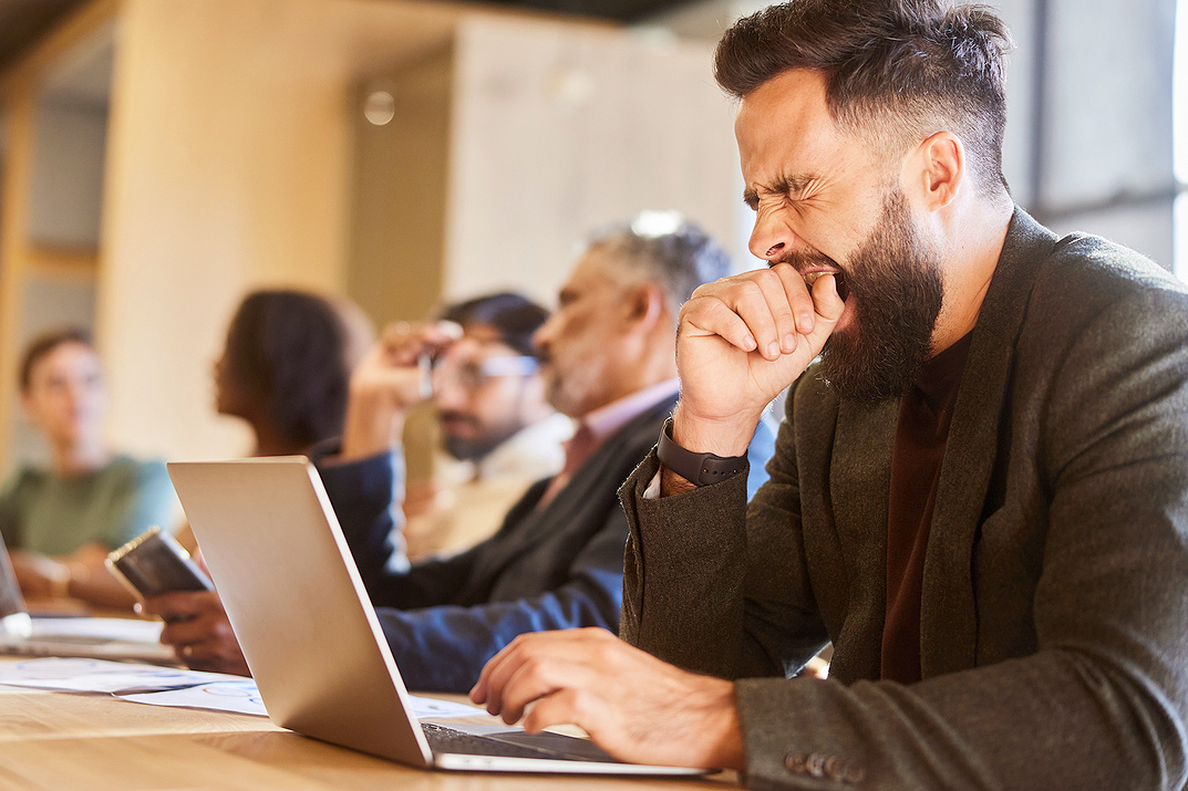 An image of a man yawning while on the computer