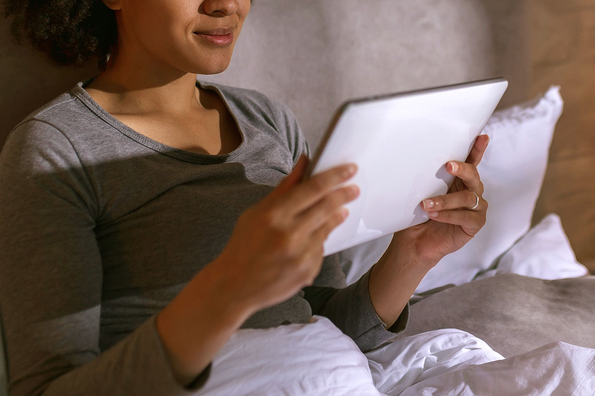 An image of a woman in bed looking at a tablet