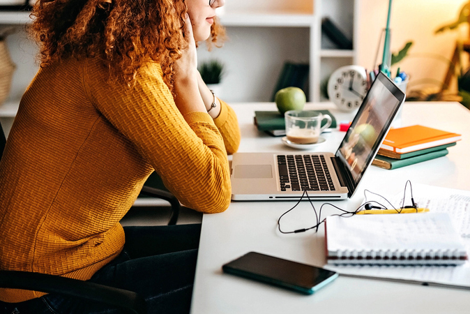 An image of a woman sitting at a desk looking at laptop