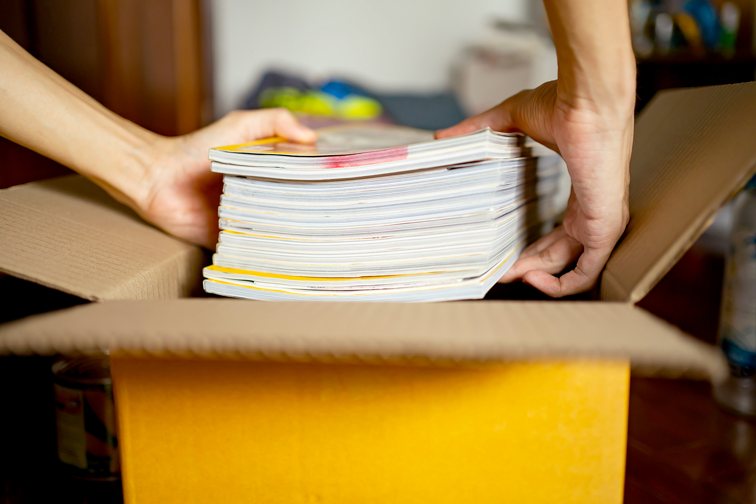 An image of person putting a stack of magazines in a box