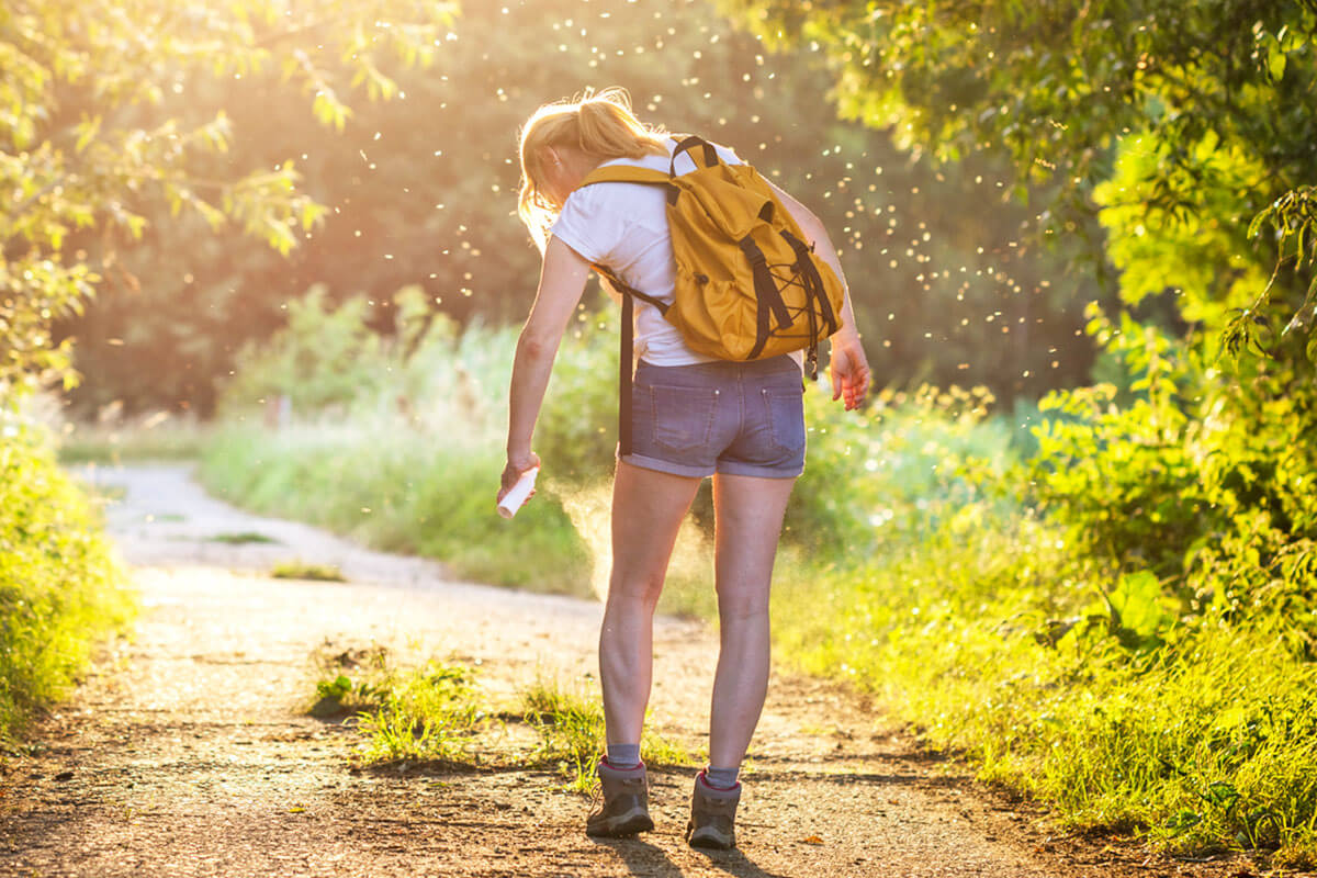 Woman with a backpack spraying bug spray to keep bugs away