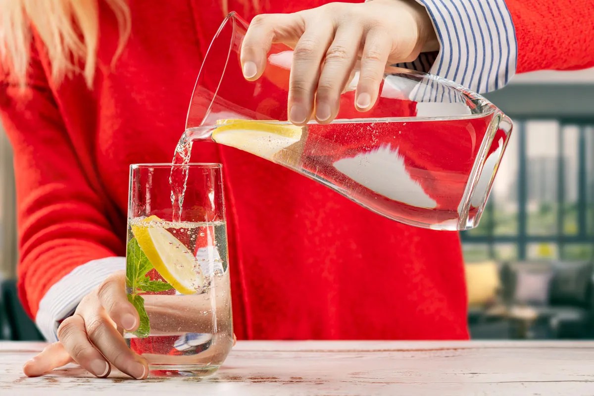 Woman pouring water from a jug into a glass.