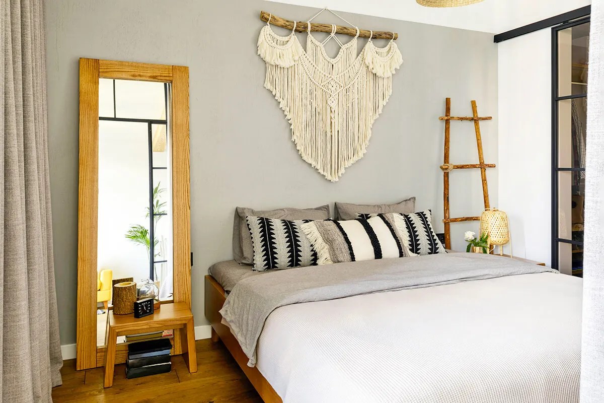 Made bed with tall mirror next to it and macrame wall art