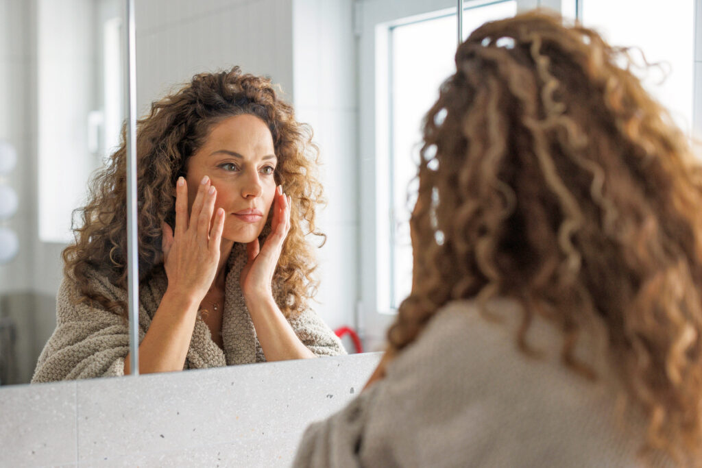 Woman looking in mirror touching face
