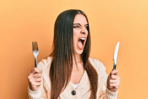 Angry woman holding knife and fork