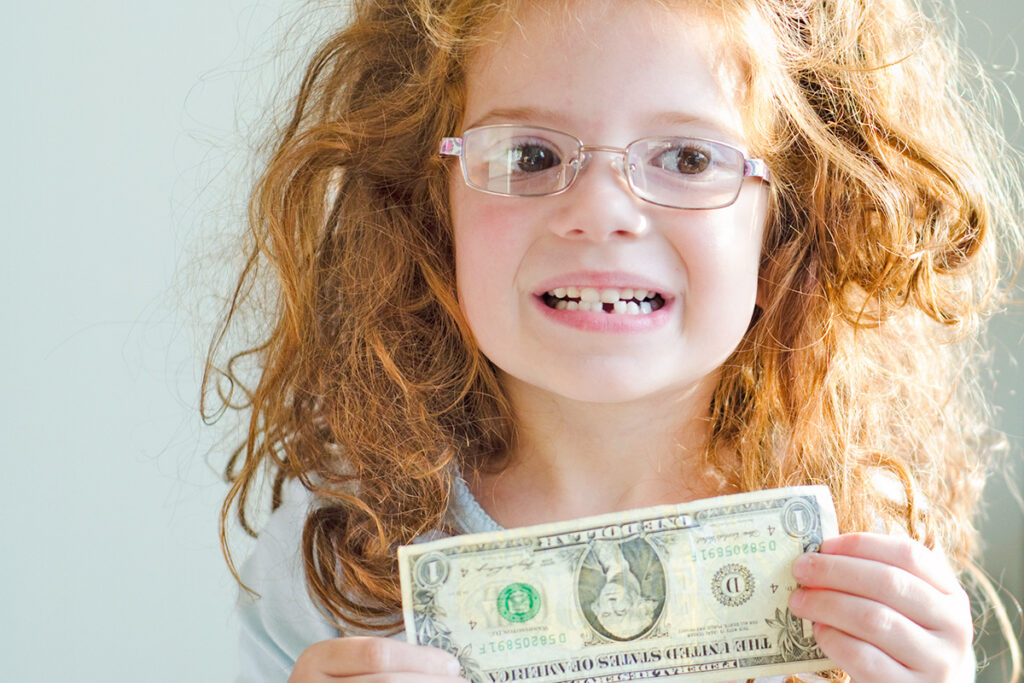 Child missing tooth holding a dollar bill