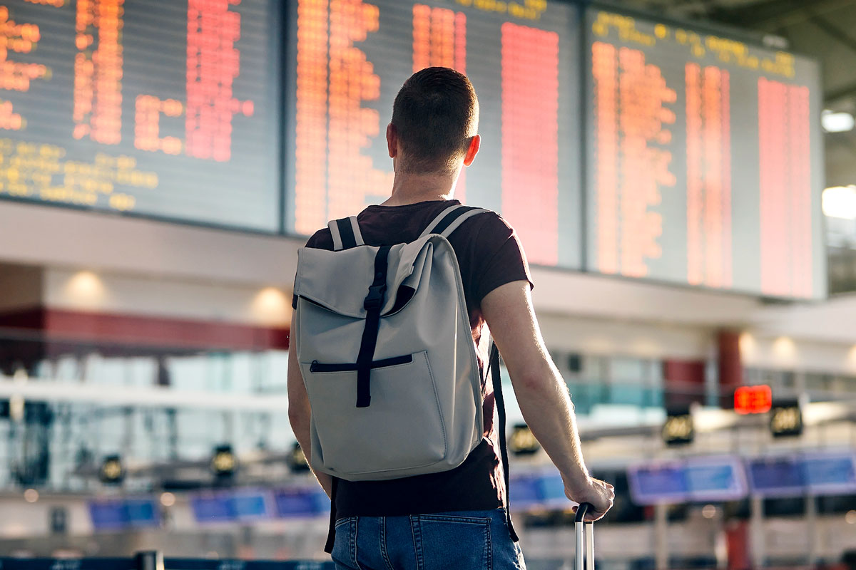 Man at airport standing before board with departures and arrivals.
