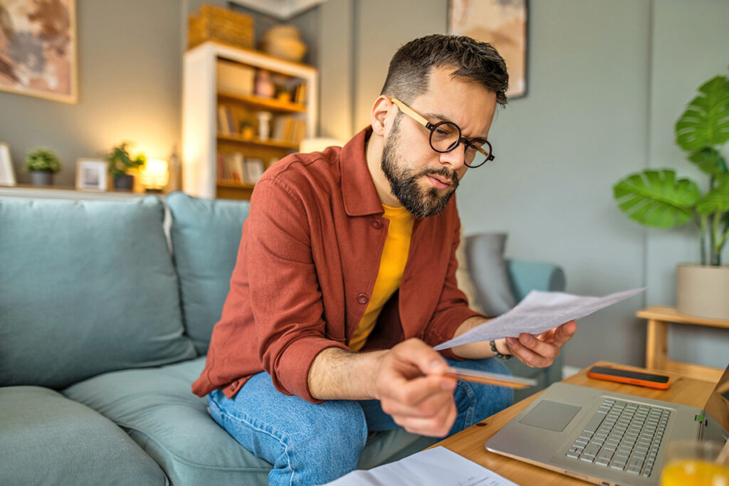 Man looking at paper in front of laptop