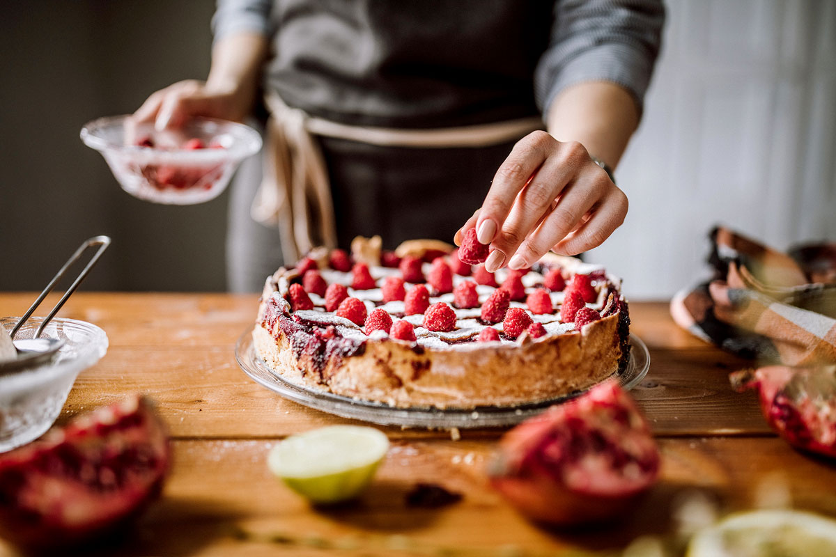 Person placing raspberry on a cake
