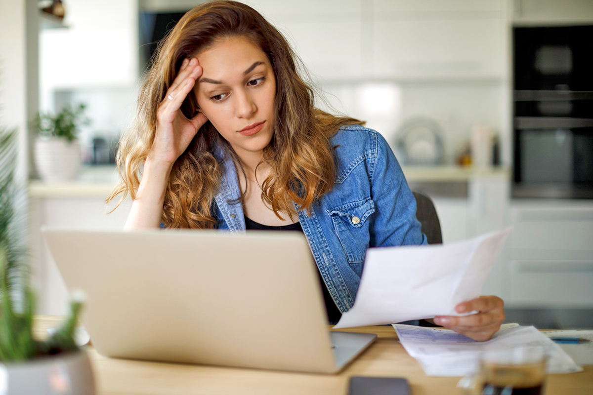 Woman with hand to forehead holding papers and looking at a computer