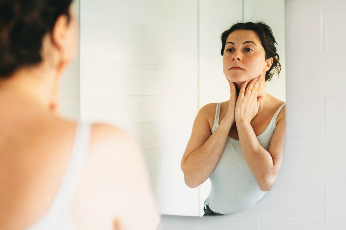 Woman looking in mirror touching neck