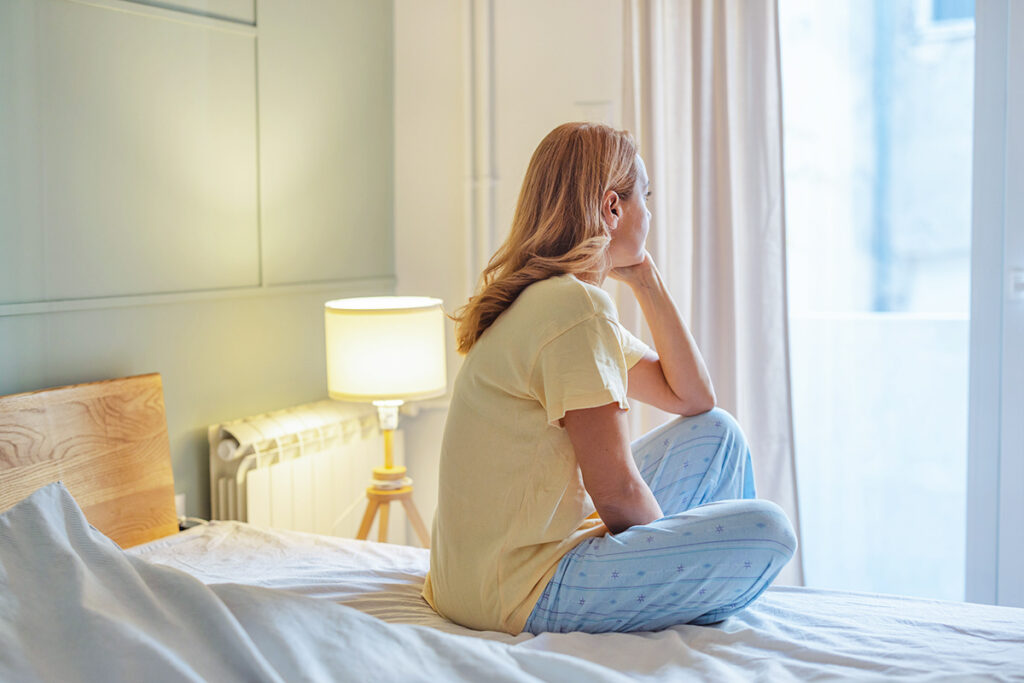 Woman sitting on bed looking out window