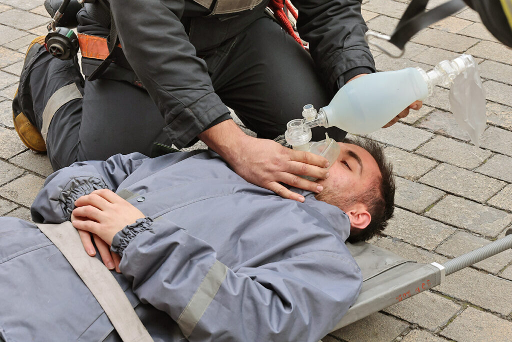 Firefighter putting oxygen bag over mouth of man on the ground